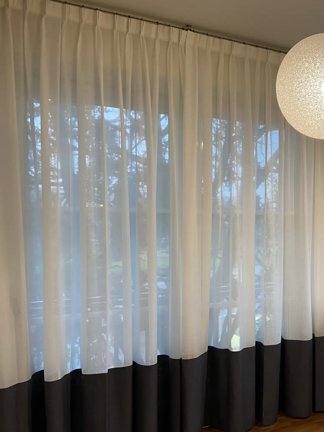 Tende in tessuto leggero bianco con la fascia scura in basso, davanti a una vetrata sul giardino